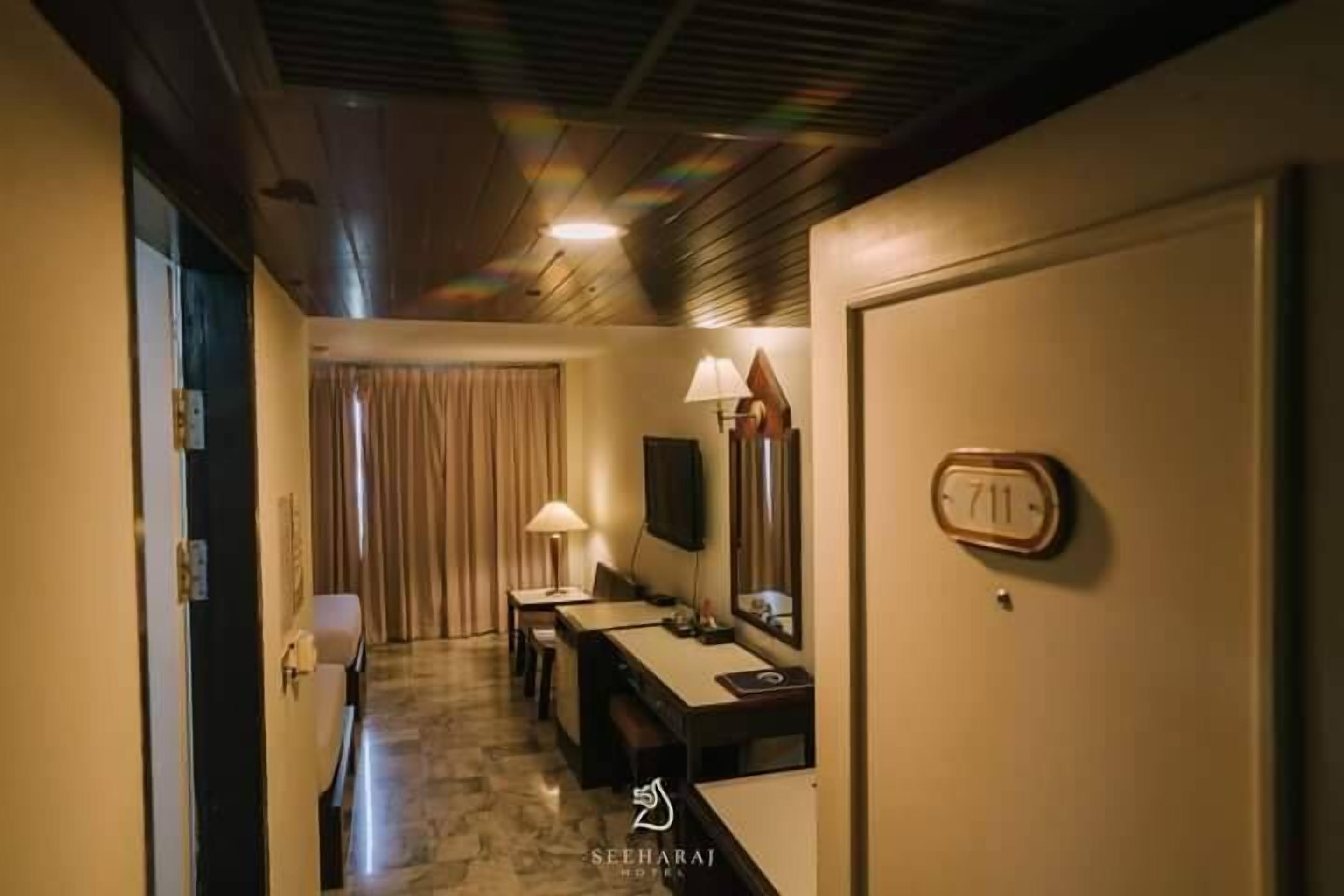 Habitación de hotel con techo de madera, un escritorio con lámpara, un televisor y una puerta con el número 711.
