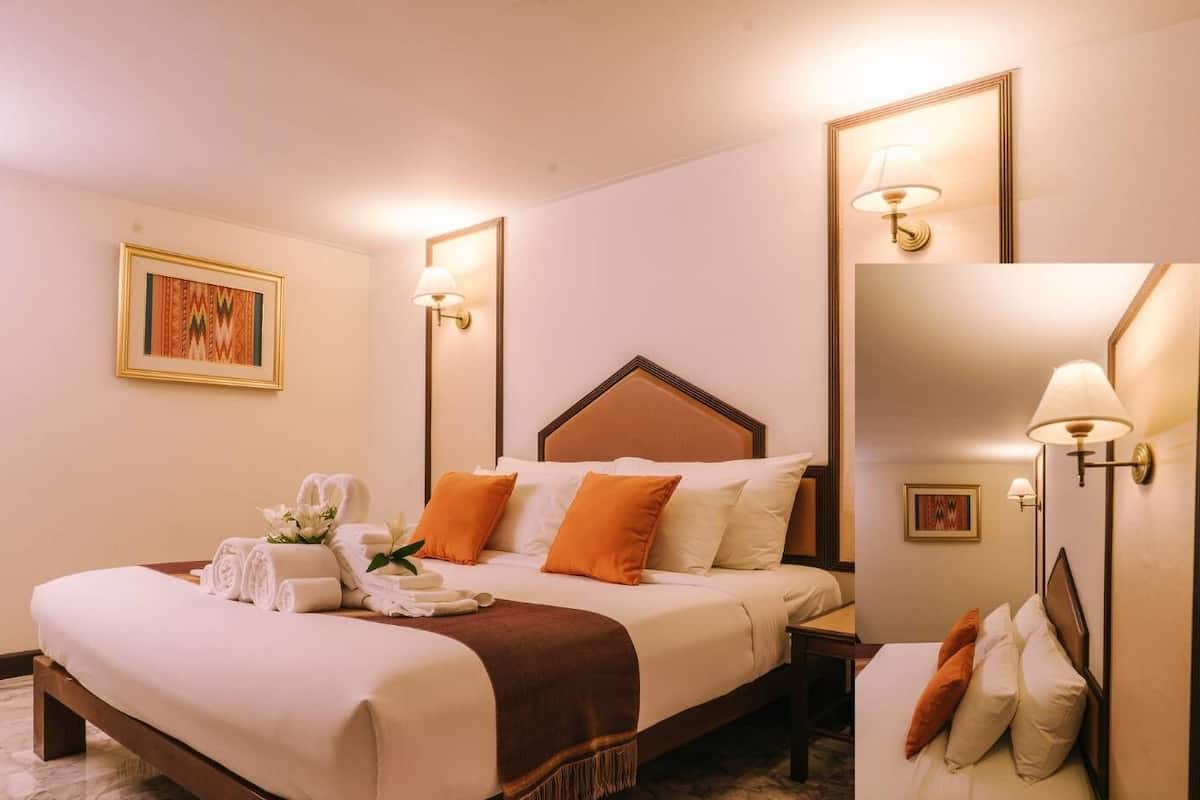 Quarto de hotel com uma cama grande, duas mesas de cabeceira, um espelho e luminárias fixadas na parede.