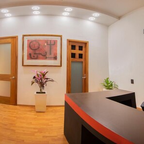 A reception area with a wooden floor, a reception desk, a framed abstract artwork, and a potted plant.