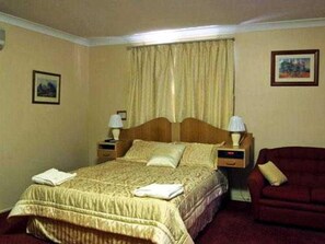A standard hotel room with a single bed, two bedside tables, a chair, and a window with curtains. - Centrepoint Motor Inn (Rockhampton)