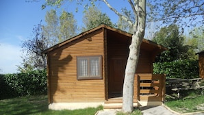 A wooden cabin with a door and window, surrounded by grass and trees. - Camping Rural Fuente de Piedra (Fuente de Piedra)