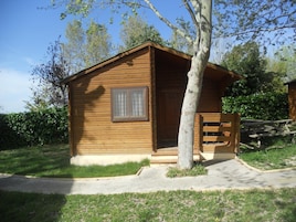 Una cabaña de madera con puerta y ventana, rodeada de hierba y árboles.