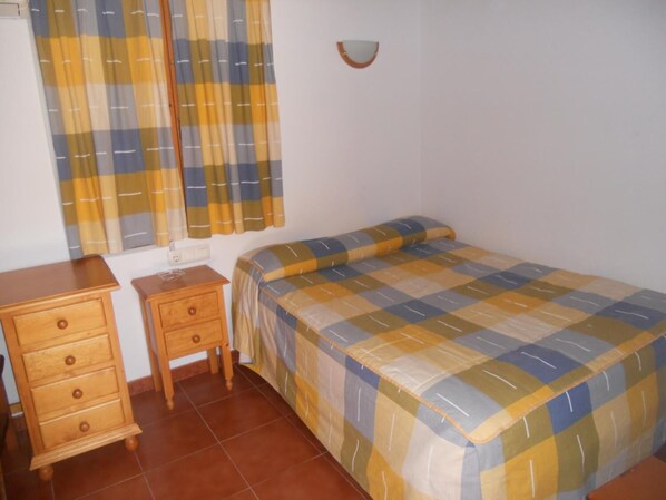 Une chambre à coucher avec un lit, une commode en bois, une table de chevet et des rideaux.
