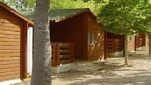 A row of wooden cabins with a dirt ground, surrounded by trees. - Camping Rural Fuente de Piedra (Fuente de Piedra)