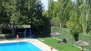 A swimming pool with a tiled deck, surrounded by a grassy area and trees. - Camping Rural Fuente de Piedra (Fuente de Piedra)