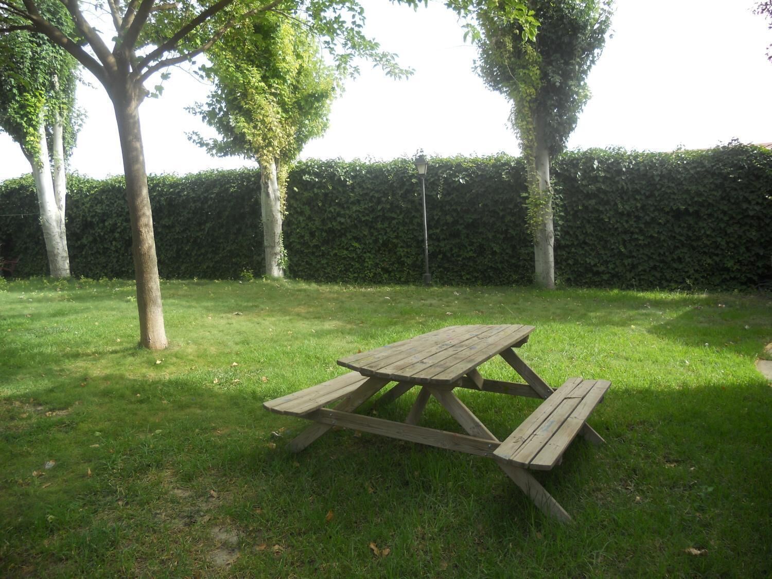 Una mesa de picnic en un área cubierta de césped, con árboles y un seto al fondo.