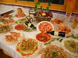 Una mesa con diversos alimentos, incluyendo platos de carne y verduras en rodajas, y una botella de vino.