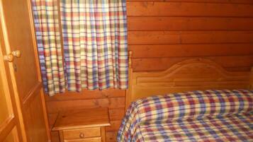 Una habitación de cabaña de madera con una cama, una mesita de noche de madera y cortinas a cuadros.