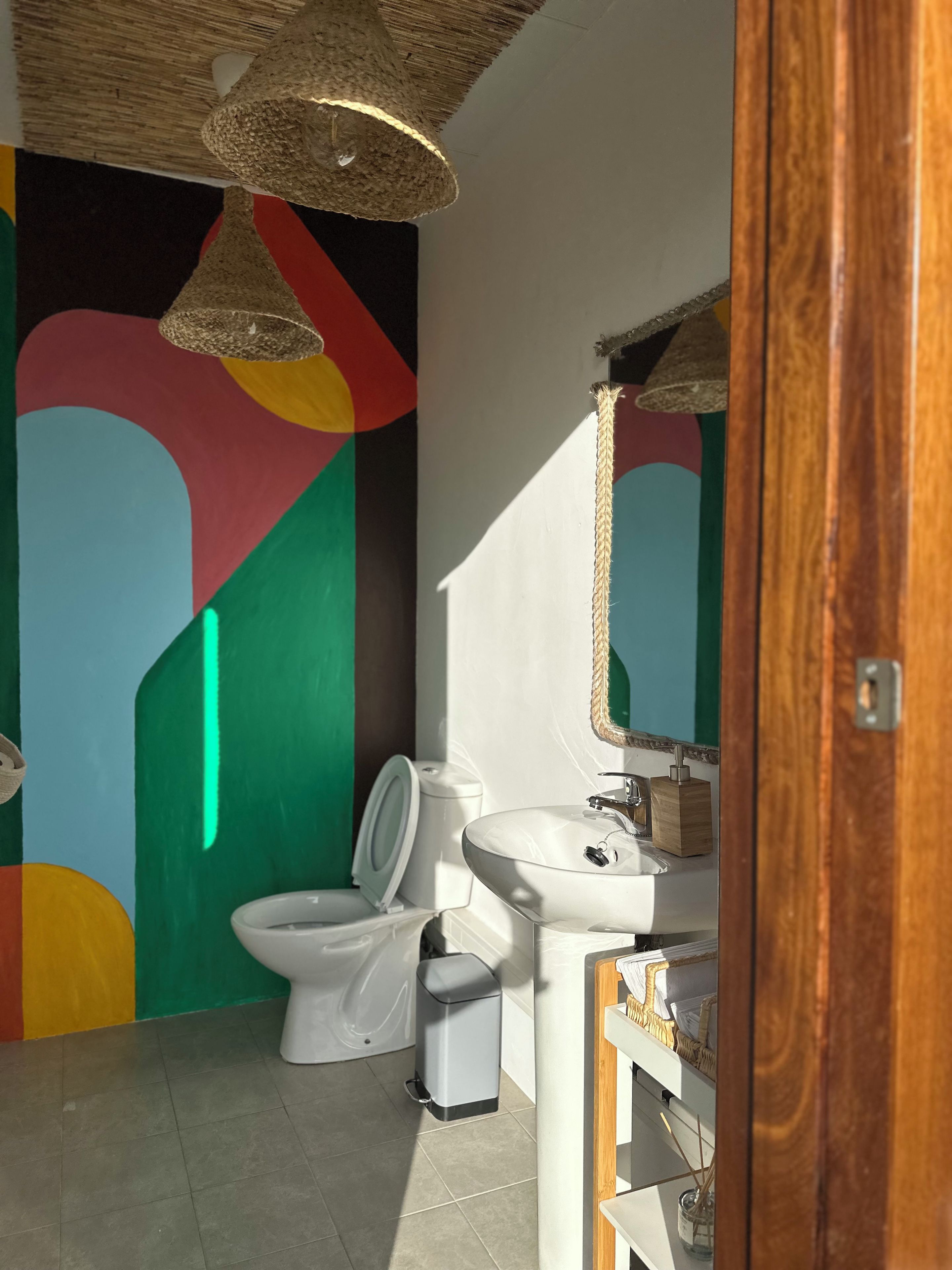 Un baño con inodoro, lavabo, bidé y un espejo, con una lámpara en el techo.