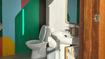 Un baño con inodoro, lavabo, bidé y un espejo, con una lámpara en el techo.