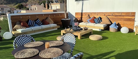 Een terras met een tafel, stoelen, een bank en een houten wand.