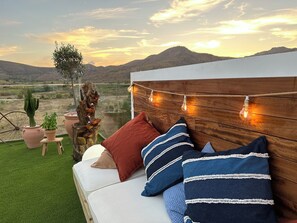 A cozy outdoor seating area with a wooden headboard, string lights, and a view of a mountainous landscape. - Hotel Portmán (La Union)