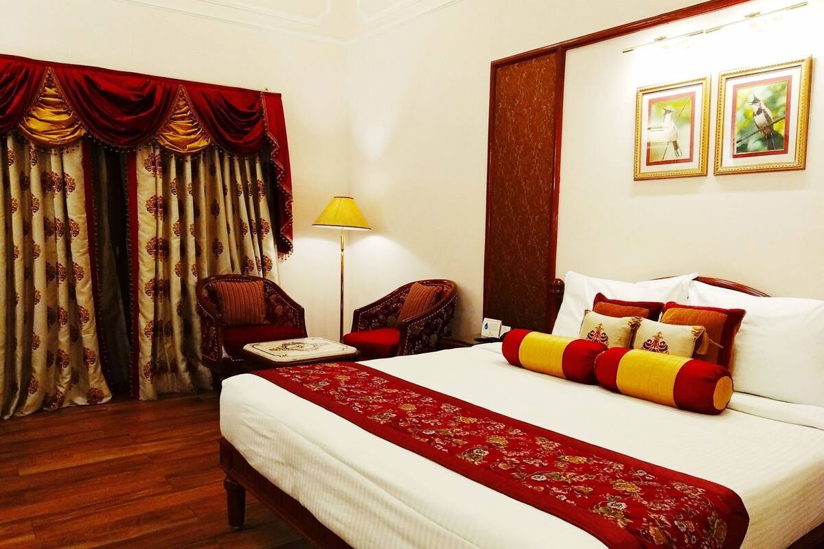 Une chambre d’hôtel avec un grand lit, une chaise, une lampe et des rideaux.