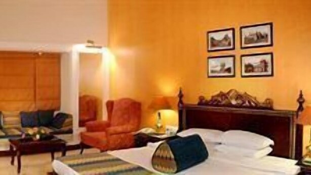 Una habitació d'hotel amb un llit, una cadira, un escriptori, una làmpada i un armari.