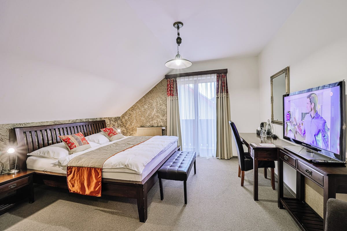 A hotel room with a large bed, a desk, a television, and a window with curtains.