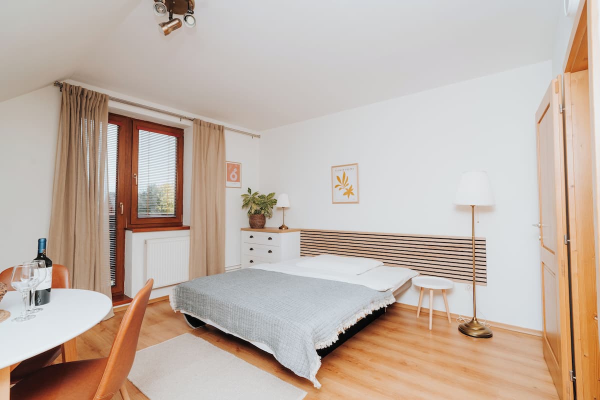 A bedroom with a bed, bedside table, lamp, and a window with curtains.