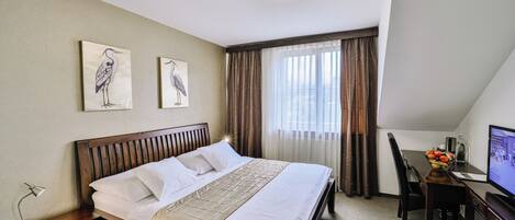 Habitación de hotel con cama, escritorio con computadora, silla, mesita de noche y dos cuadros de aves colgados en la pared.