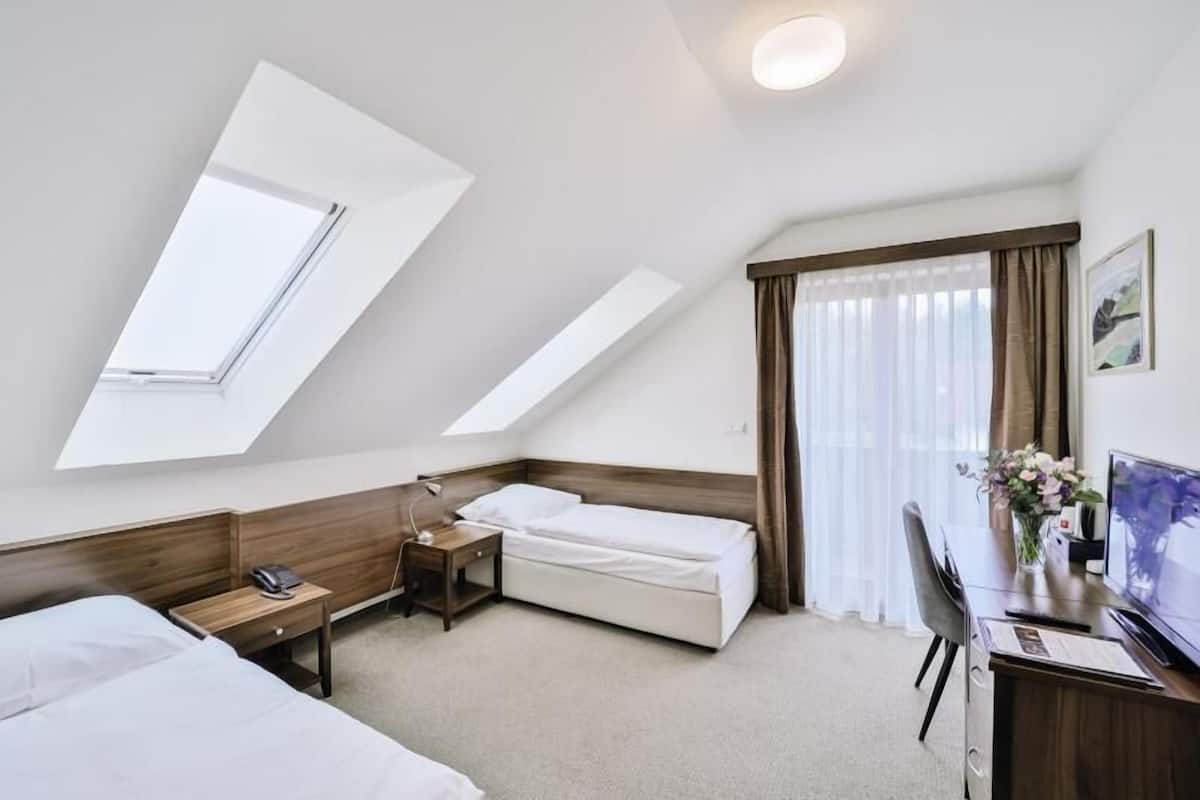 A hotel room with two beds, a desk with a computer, a chair, a small table with a lamp, and a window with curtains.
