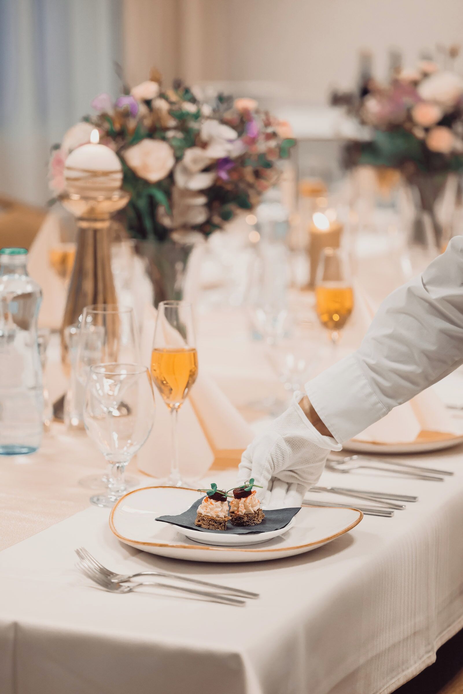 A table set for a meal with a dessert plate, glasses, and a vase of flowers.