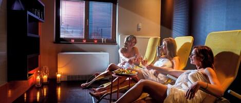 A room with reclining chairs, a window with blinds, a radiator, and candles on the floor.