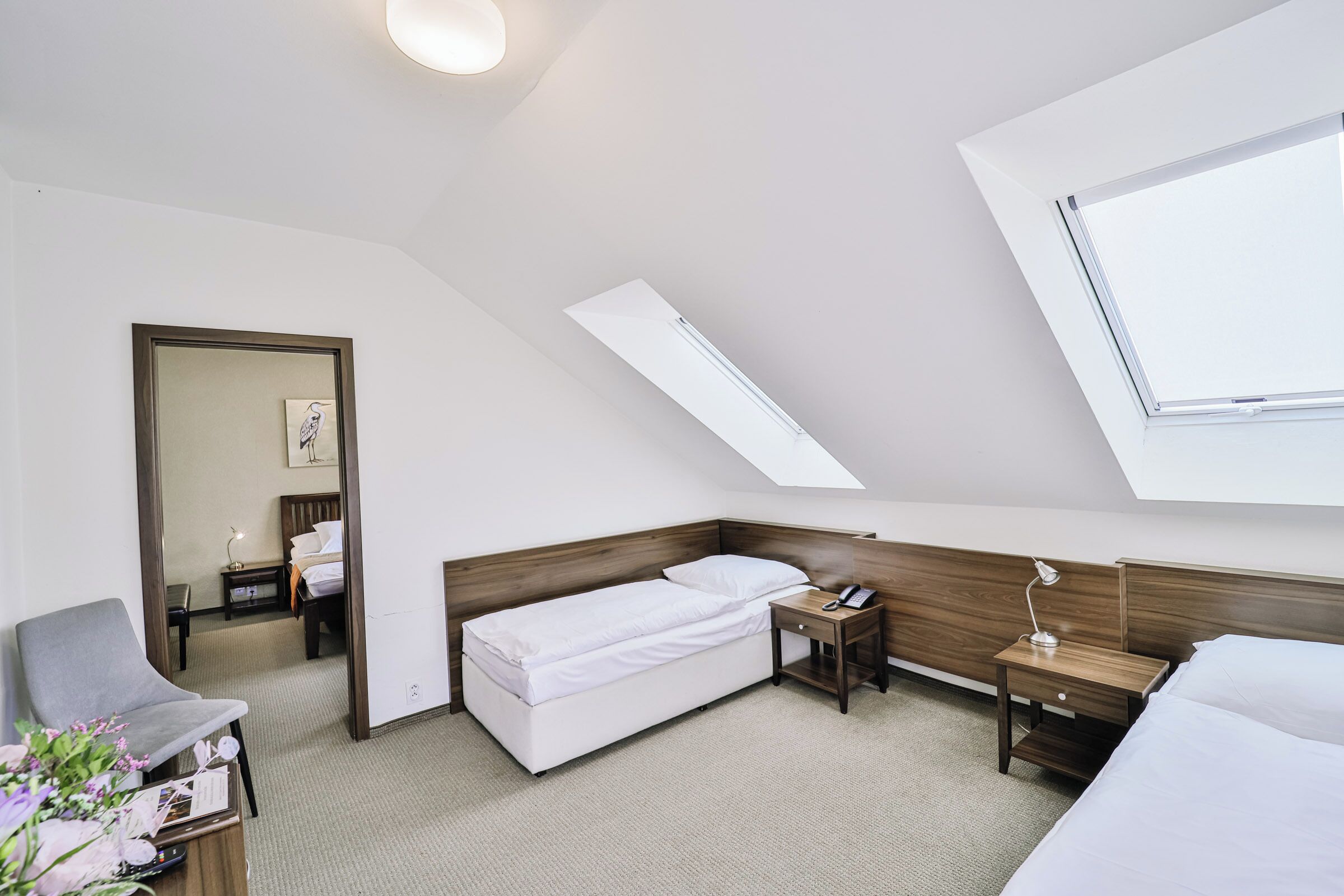A modern hotel room with a skylight, a single bed, a desk with a lamp, and a chair.