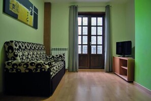 Una sala de estar con un sofá estampado, un televisor sobre un mueble de madera y un ventanal con cortinas.