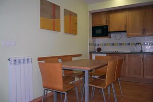 Un comedor con mesa y sillas, una cocina con armarios de madera y salpicadero de azulejos.