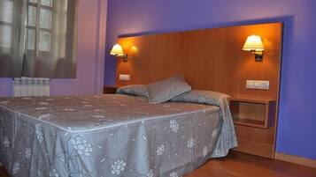 Un dormitorio con cama, dos lámparas de noche, cabecera y ventana con persianas.