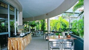 An outdoor dining area with a covered section, tables, chairs, and a buffet setup. - The Leela Resort & Spa Pattaya (Pattaya)
