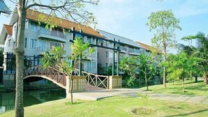 A multi-story building with a bridge over a water body, surrounded by greenery and palm trees. - The Leela Resort & Spa Pattaya (Pattaya)