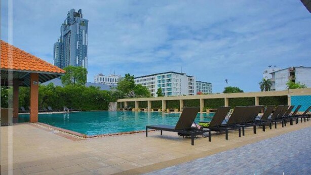 A swimming pool with lounge chairs, a covered seating area, and modern buildings in the background. - The Leela Resort & Spa Pattaya (Pattaya)