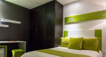 Una habitación de hotel moderna con una cama grande, almohadas verdes, un escritorio con una computadora y una pared de acento verde.