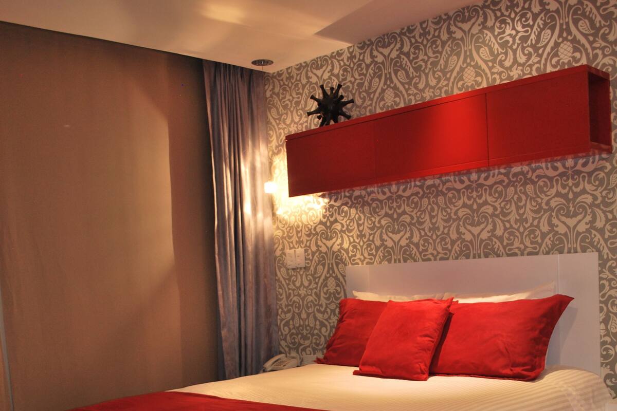 A bedroom with a large bed, a red accent wall, and a patterned wallpaper.