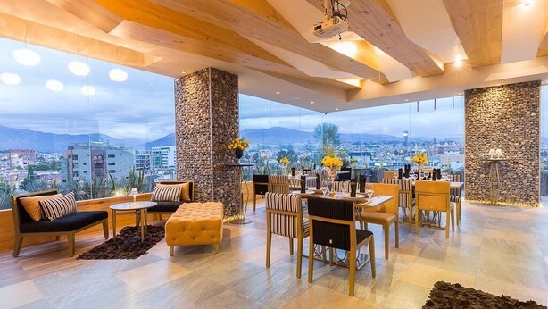 A spacious living area with a high ceiling, stone pillars, and a city view. - Rioné Hotel Boutique (Cuenca)