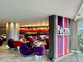Un interior moderno con un letrero destacado que dice 'Rijone', zonas de estar con sillas moradas y rojas, y un diseño de pared con motivos geométricos.