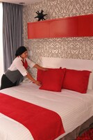 Una habitación de hotel con cama, almohadas rojas, cabecero rojo y papel tapiz estampado.