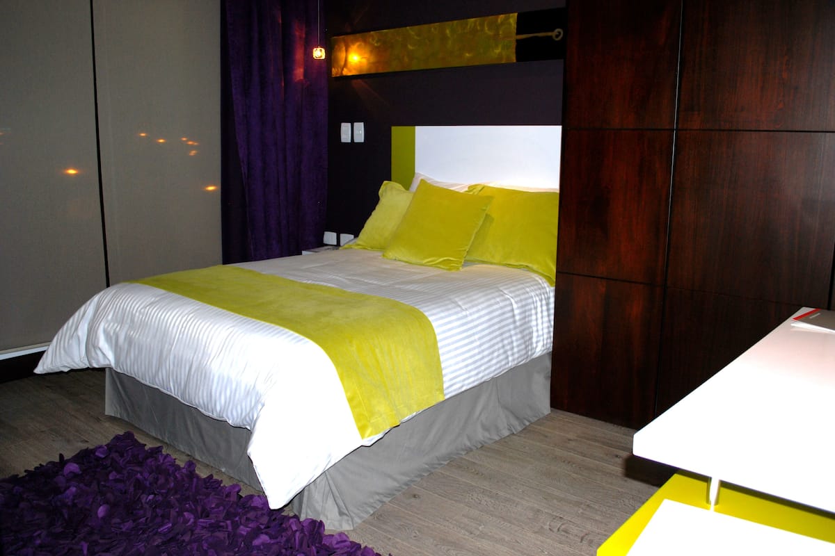 A modern bedroom with a bed, a bedside table, and a purple rug.