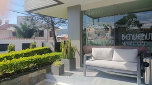 A modern outdoor seating area with a white sofa and a glass wall displaying a welcome message. - Rioné Hotel Boutique (Cuenca)