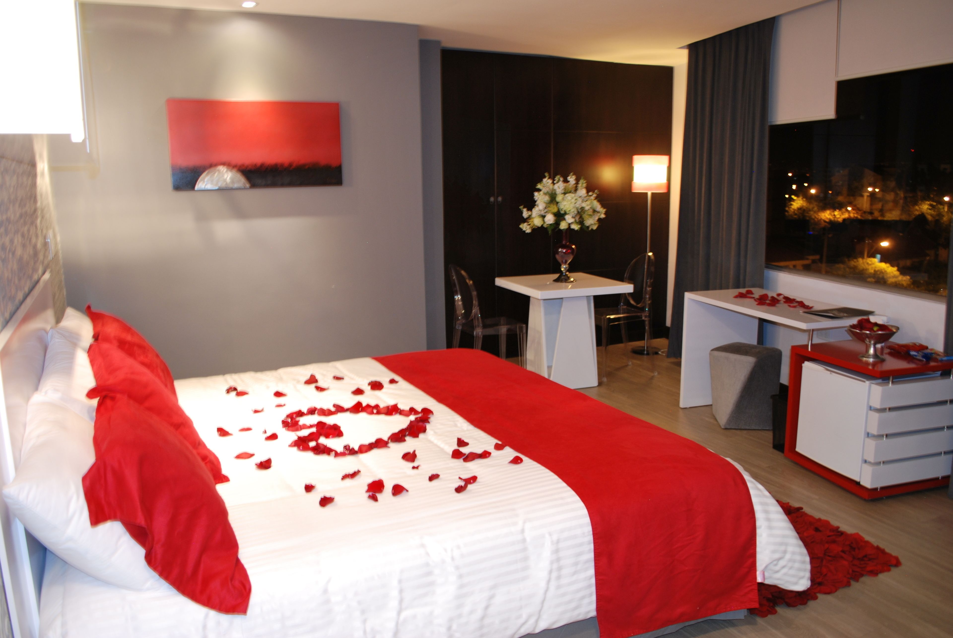 A hotel room with a bed, a desk, a chair, a lamp, and a window with a view of the city at night.
