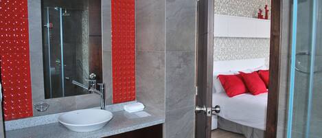 Un baño moderno con cabina de ducha de vidrio, un lavamanos blanco y una pared de acento roja.