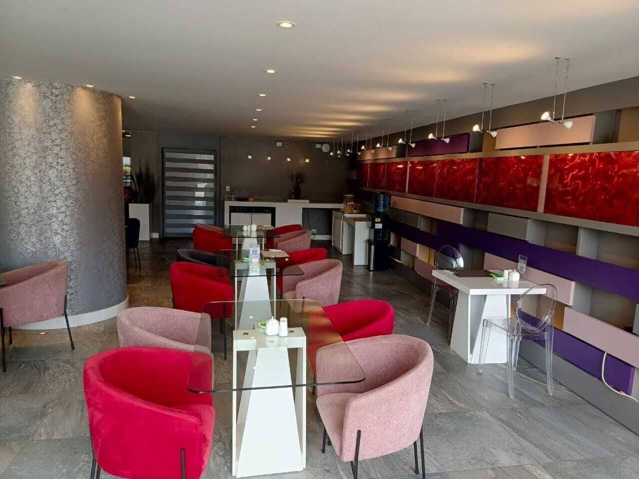 Un interior moderno con sillas rojas y rosadas, una mesa de cristal y una zona de bar con una paleta de colores rojo y morado.