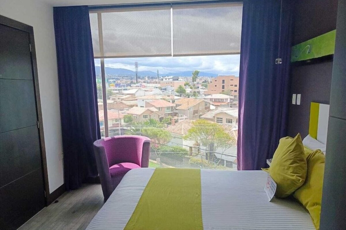Une chambre d’hôtel avec un lit, une chaise et une grande fenêtre donnant sur la ville.