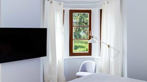 A room with a bed, a chair, a TV, a window with curtains, and a desk lamp. - Villa Riedenburg Design Apartments (Salzburg)