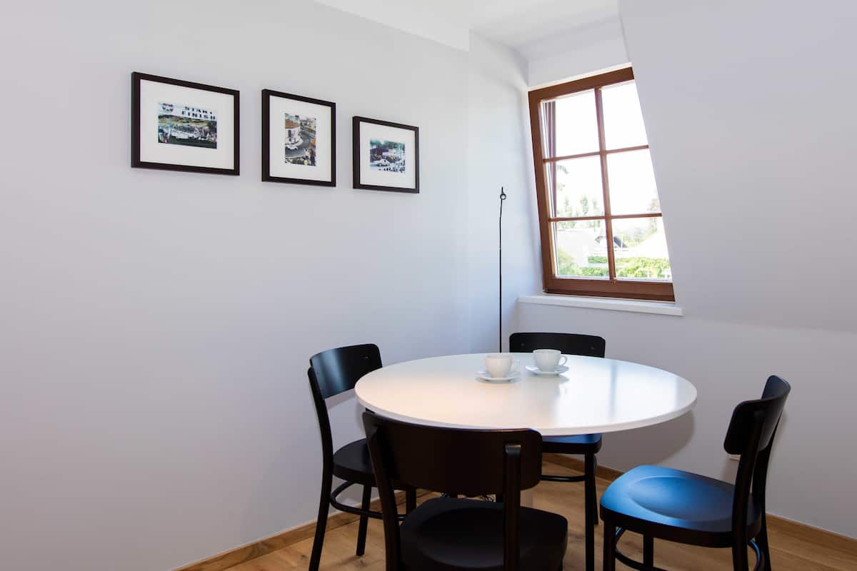 Uma pequena área de refeições com uma mesa redonda, quatro cadeiras e três fotografias emolduradas na parede.