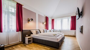 A modern bedroom with a large bed, bedside tables, a TV, and a window with curtains.
