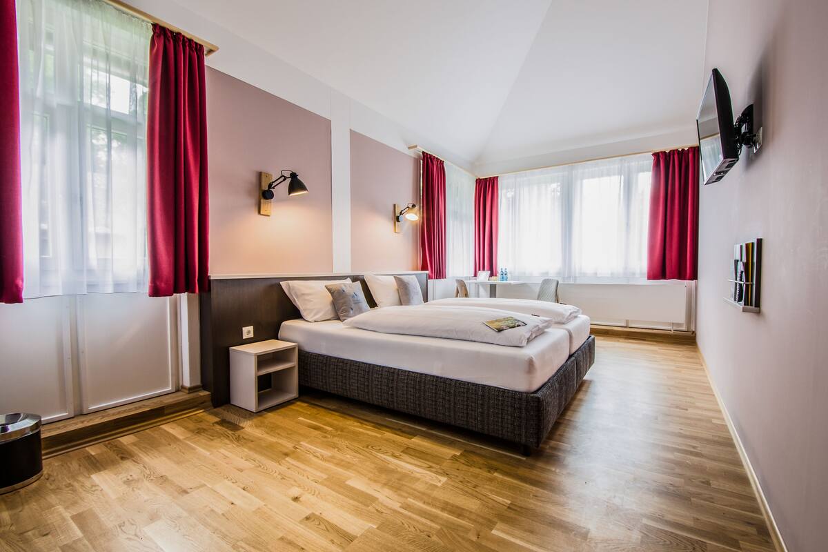 A modern bedroom with a large bed, bedside tables, a TV, and a window with curtains.