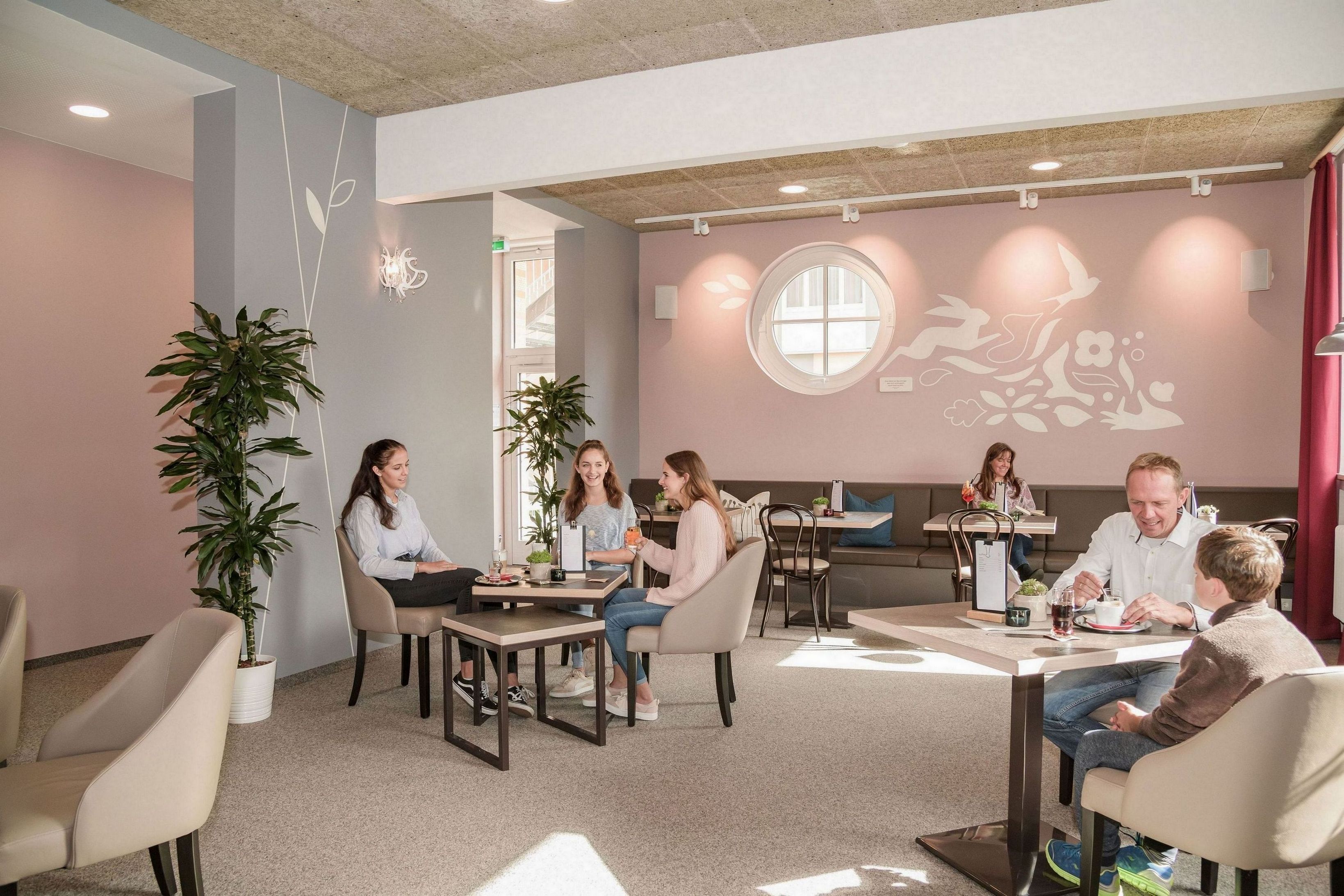 A modern interior with a group of people seated at a table, a large window, and potted plants.