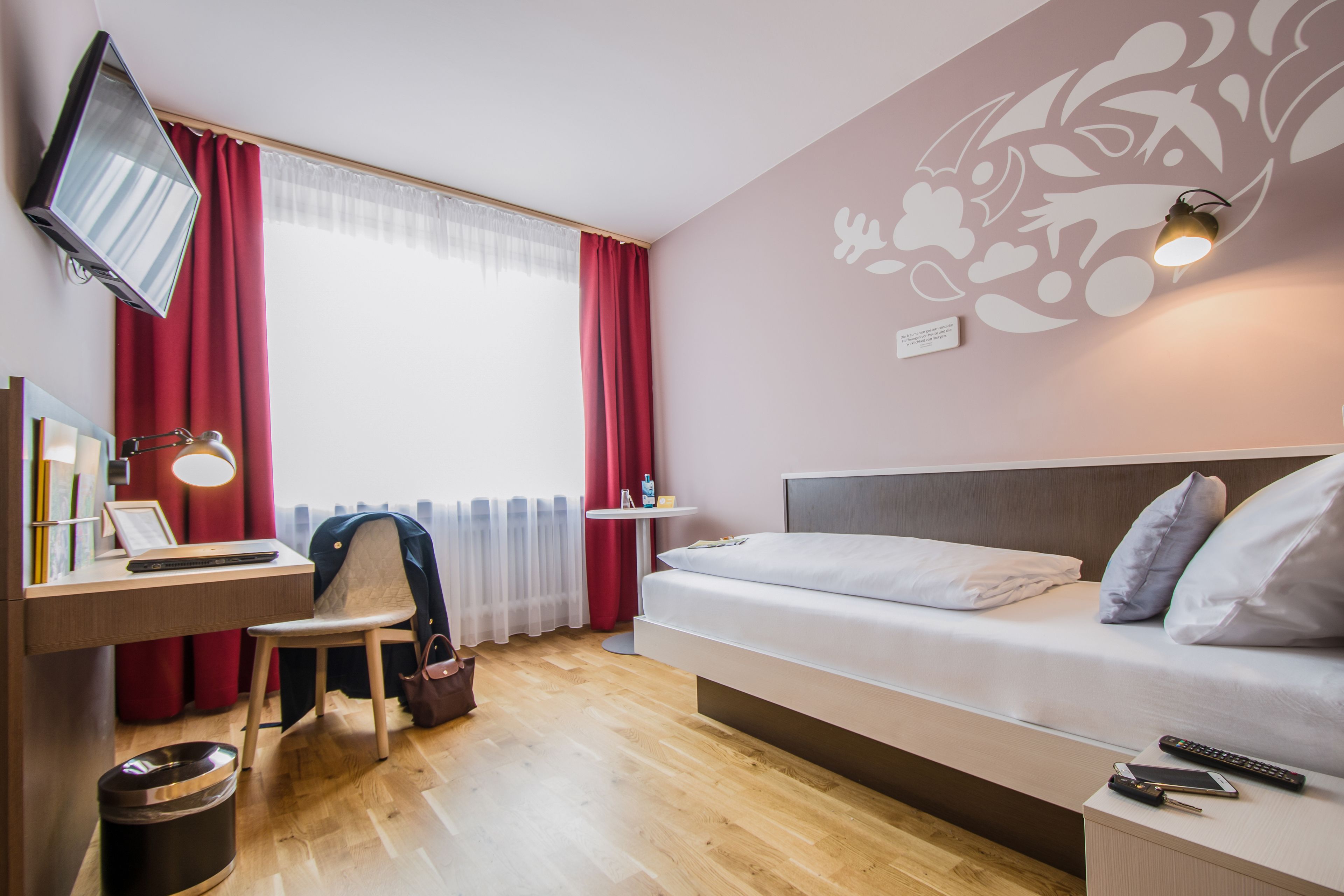 Una habitación de hotel moderna con cama, escritorio, silla y televisor montado en la pared.