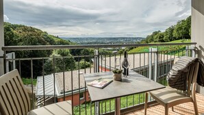 A balcony with a table, chairs, and a bottle of wine.