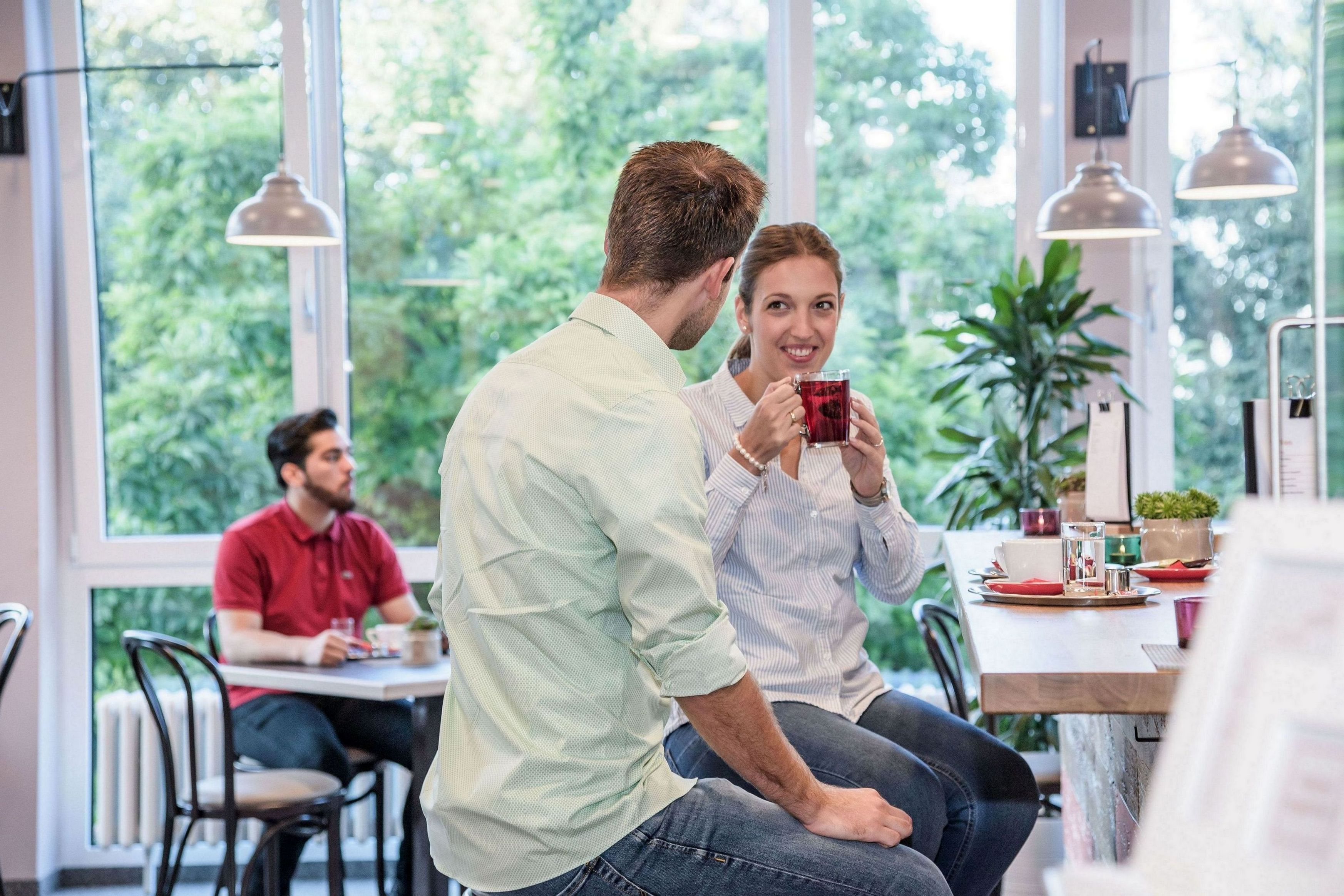 A dining area with large windows, a table with chairs, and a person holding a red cup.